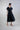 Vestido midi con cintura fruncida y detalle escultórico en movimiento, mostrando la caída del tejido y la definición de la silueta al caminar.