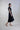 Vista lateral de vestido midi con cintura fruncida y detalle escultórico, destacando la estructura de la silueta y la caída natural del tejido en perfil.