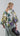 Back view of a sun-kissed floral cotton blouse with a wide boat neckline, highlighting its high-low hemline, relaxed sleeves below the elbow and softly adjustable drawstring waist.